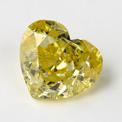 Yellow heart-shaped diamond on a pale surface, leaning slightly to one side with internal markings visible through the crown.