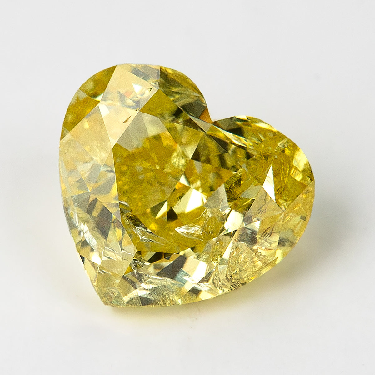 Yellow heart-shaped diamond on white, with the point angled left and a bright reflection through the lower facets.