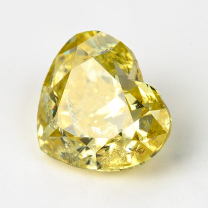 Heart-shaped yellow diamond on a pale background, showing a broad light reflection across its central table.