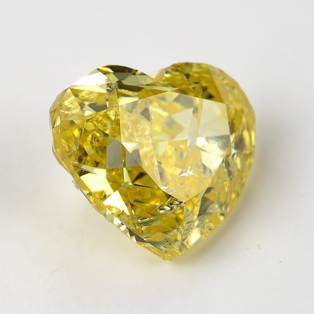 Yellow heart-shaped diamond facing upward on a pale surface, showing its rounded lobes and dark lower facet reflections.