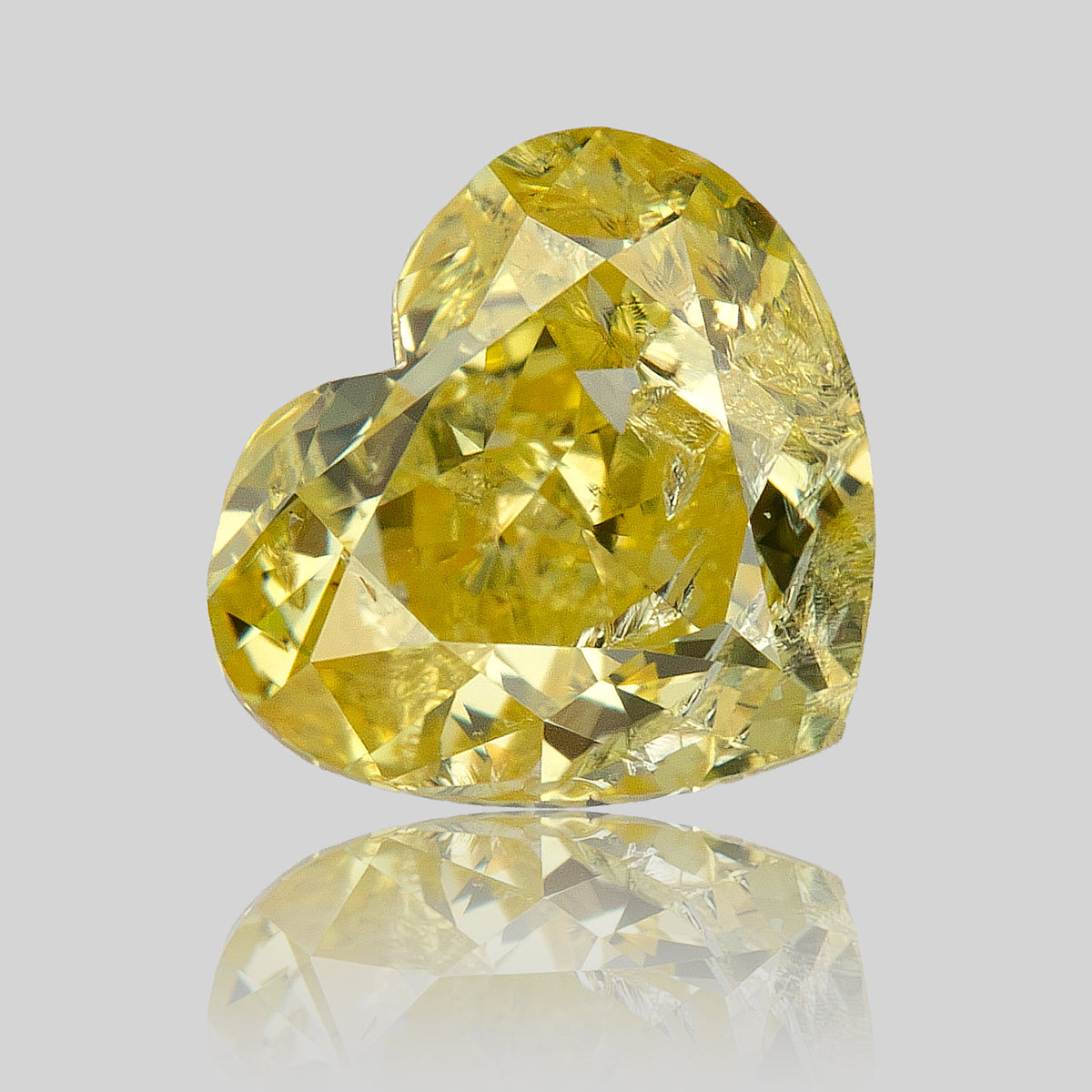 Yellow heart-shaped diamond standing at an angle on a reflective surface, with a faint mirrored outline beneath.