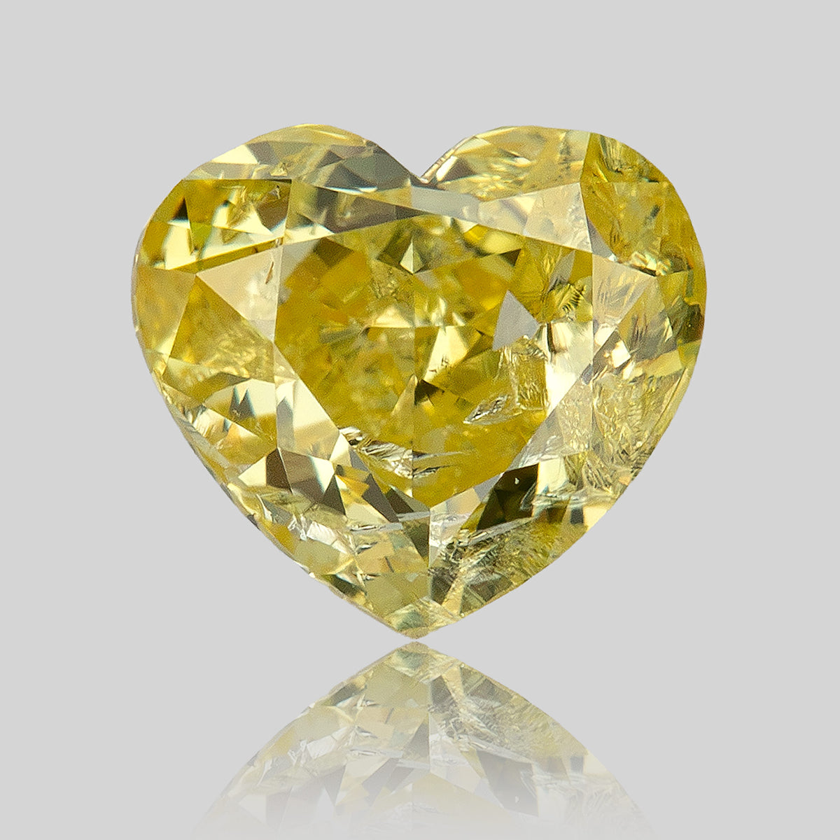 Heart-shaped yellow diamond upright on a reflective surface, with its pointed tip above a faint reflected image.