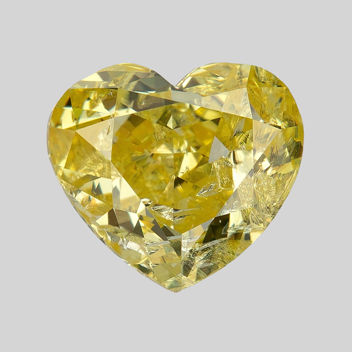 Yellow heart-shaped diamond facing upward on a pale grey background, with its cleft, pointed tip, facets and internal markings clearly visible.