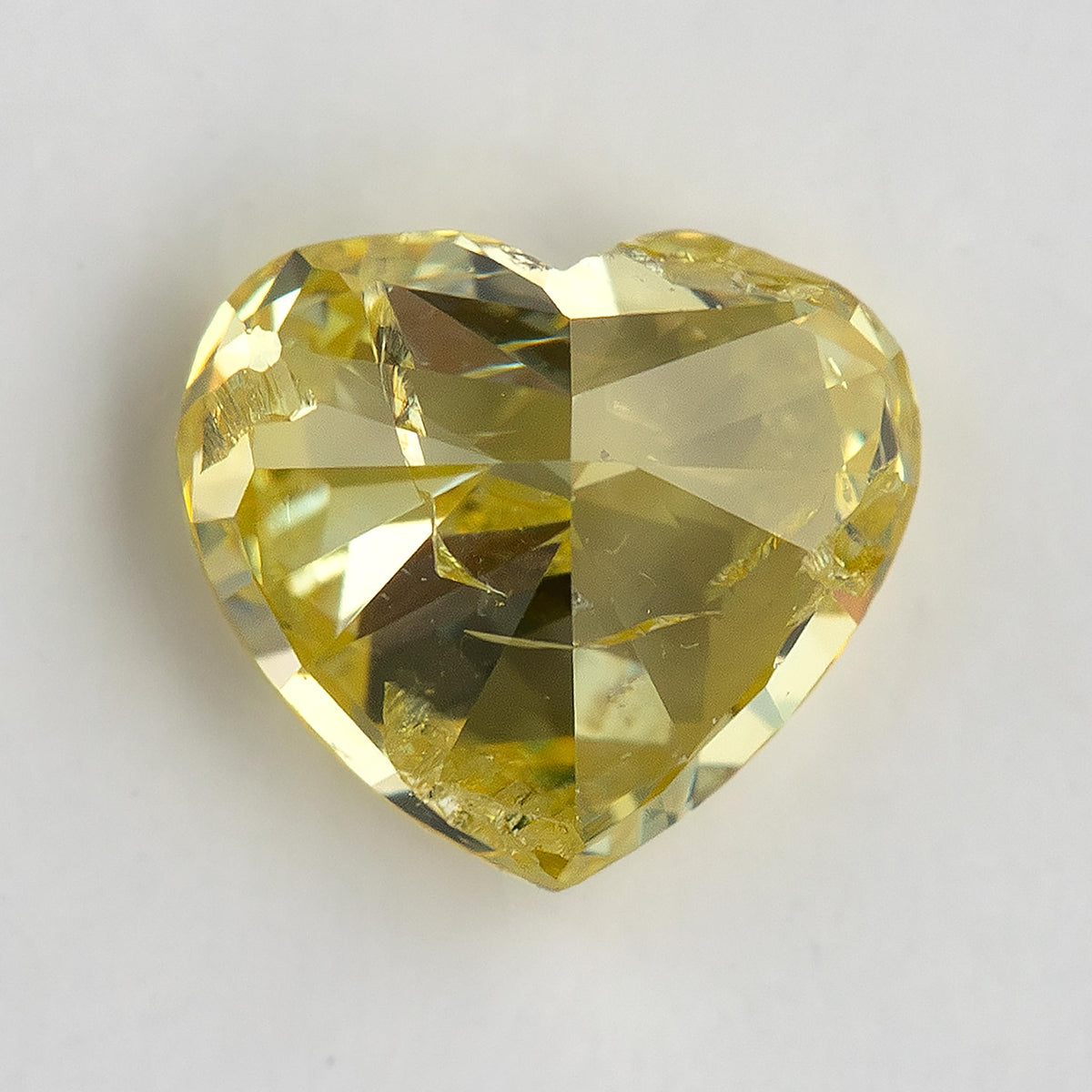 Back-facing view of the yellow heart-shaped diamond on white, with broad pavilion facets and a darker central reflection.