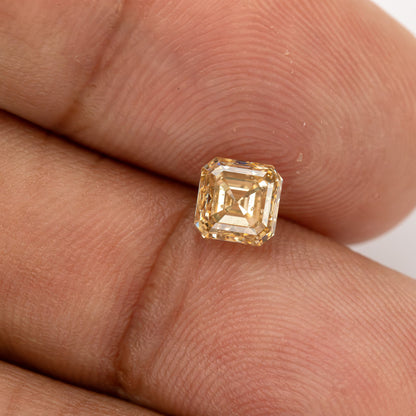 Champagne-colored square Asscher-cut diamond resting between fingertips, with warm reflections and visible internal characteristics.