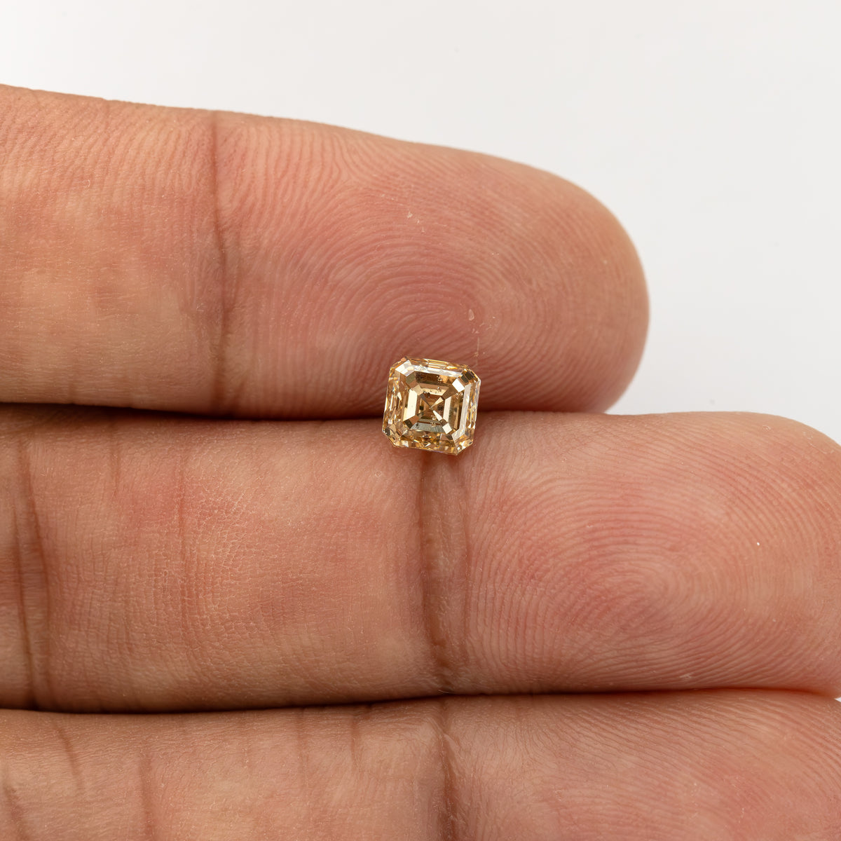 Small square Asscher-cut diamond on two fingers, with the surrounding hand showing its approximately 5 mm scale.