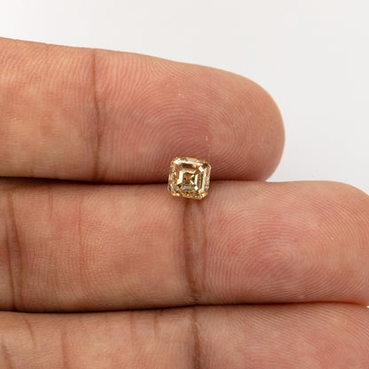 Small square Asscher-cut diamond on two fingers, with the surrounding hand showing its approximately 5 mm scale.