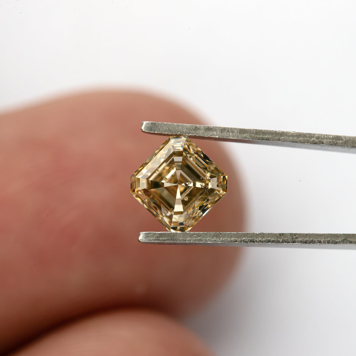 Champagne Asscher-cut diamond held diagonally between tweezers in front of a hand.