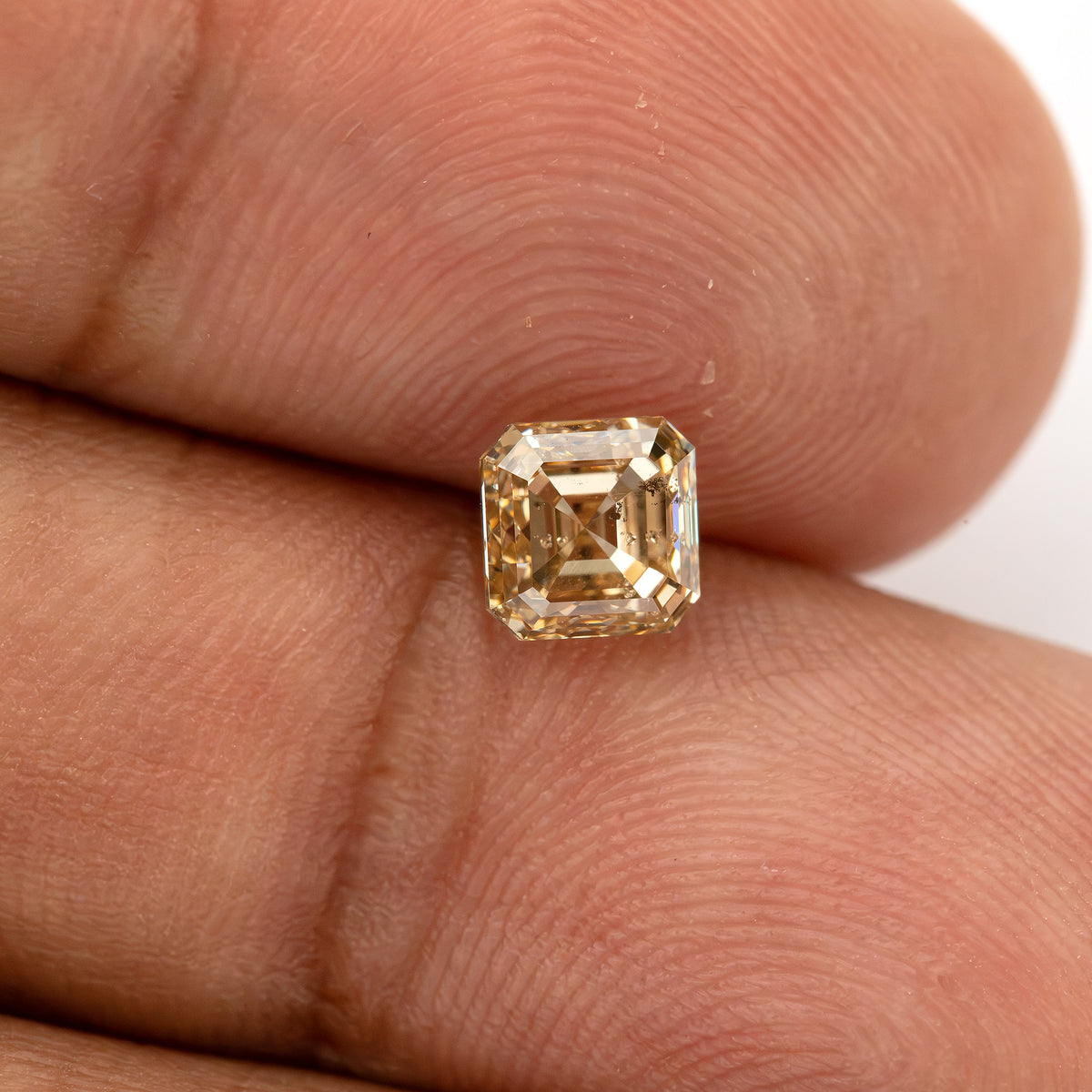 Close fingertip view of the warm-toned square diamond, with dark clarity characteristics visible through the face.