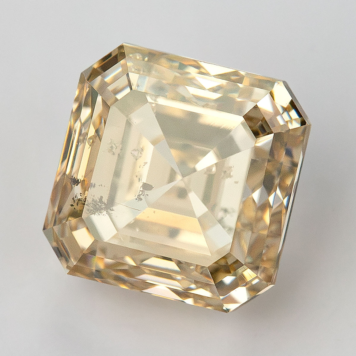 Tilted champagne diamond on a light surface, with a pale central reflection and dark characteristics near one edge.
