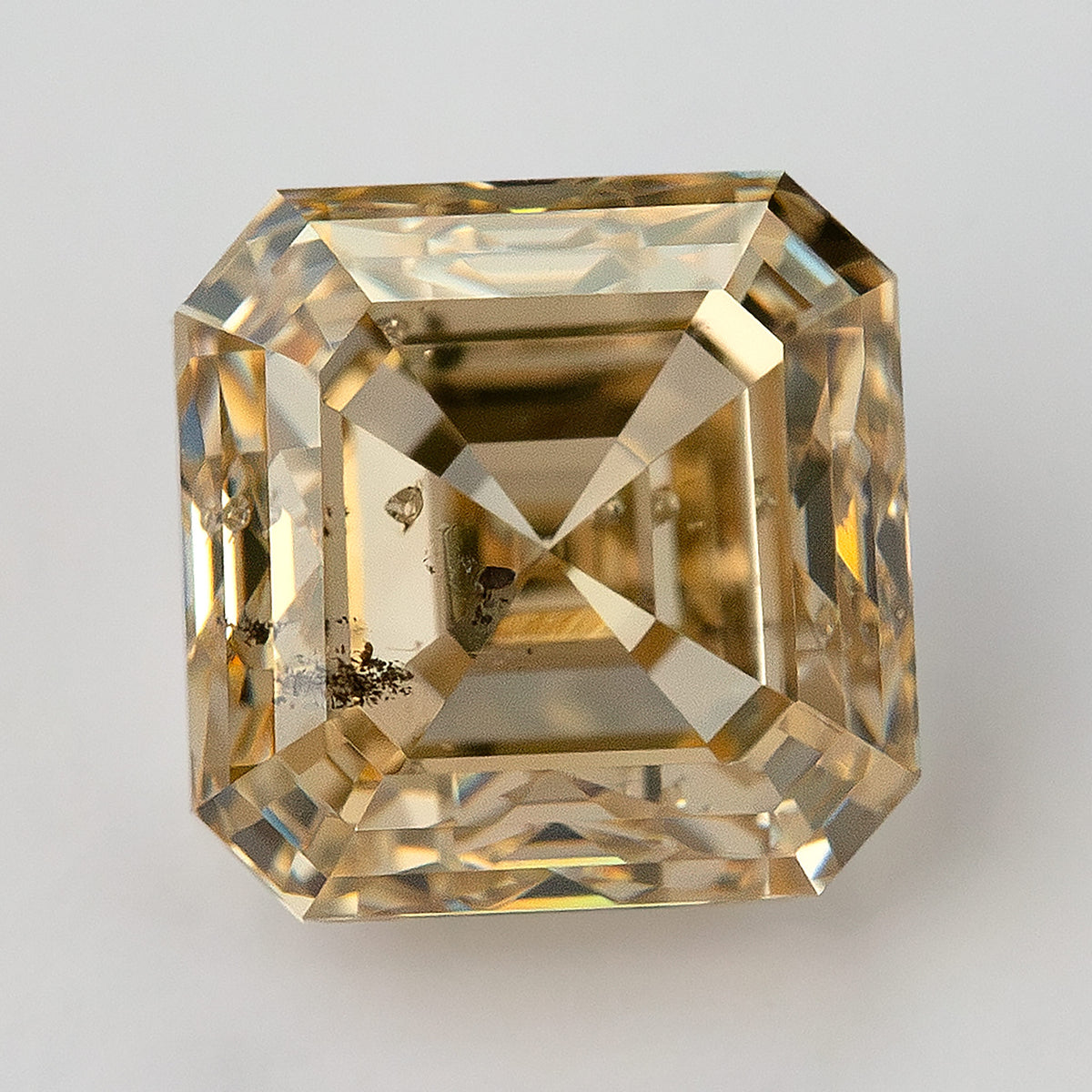 Close face-up view of the champagne Asscher-cut diamond, with dark internal features across the lower-left portion.