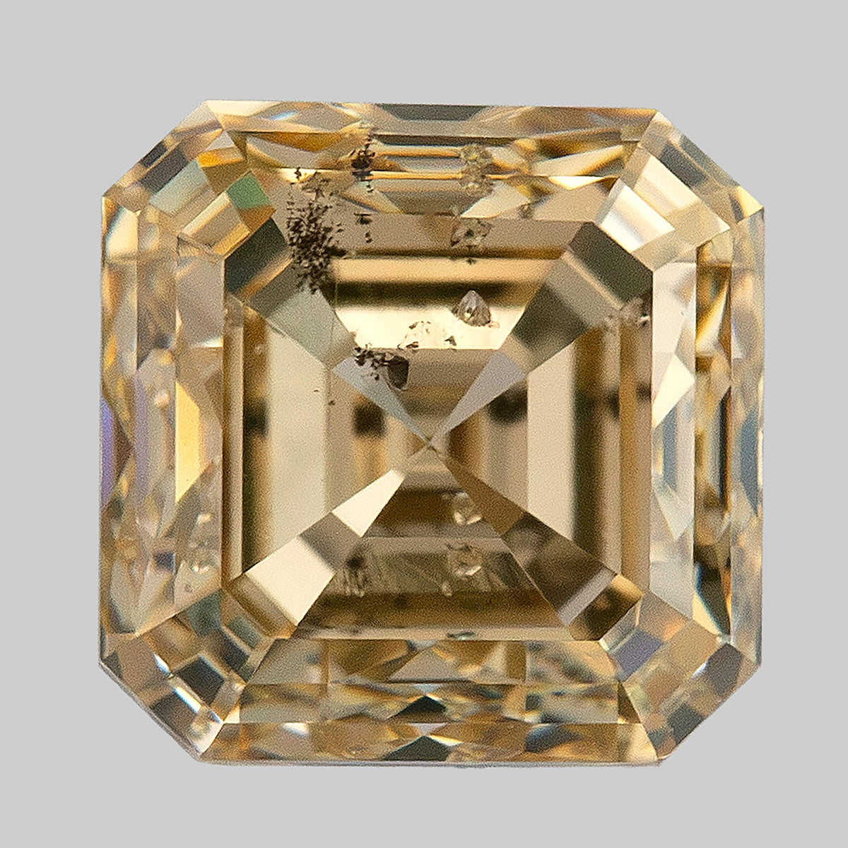 Warm face-up macro of the square diamond showing strong stepped reflections and clustered dark characteristics.