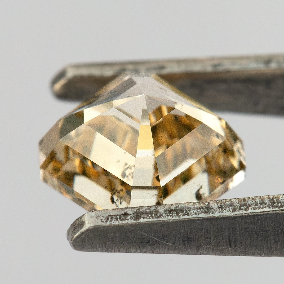 Pointed underside of the champagne diamond held between tweezers, showing angled pavilion facets.
