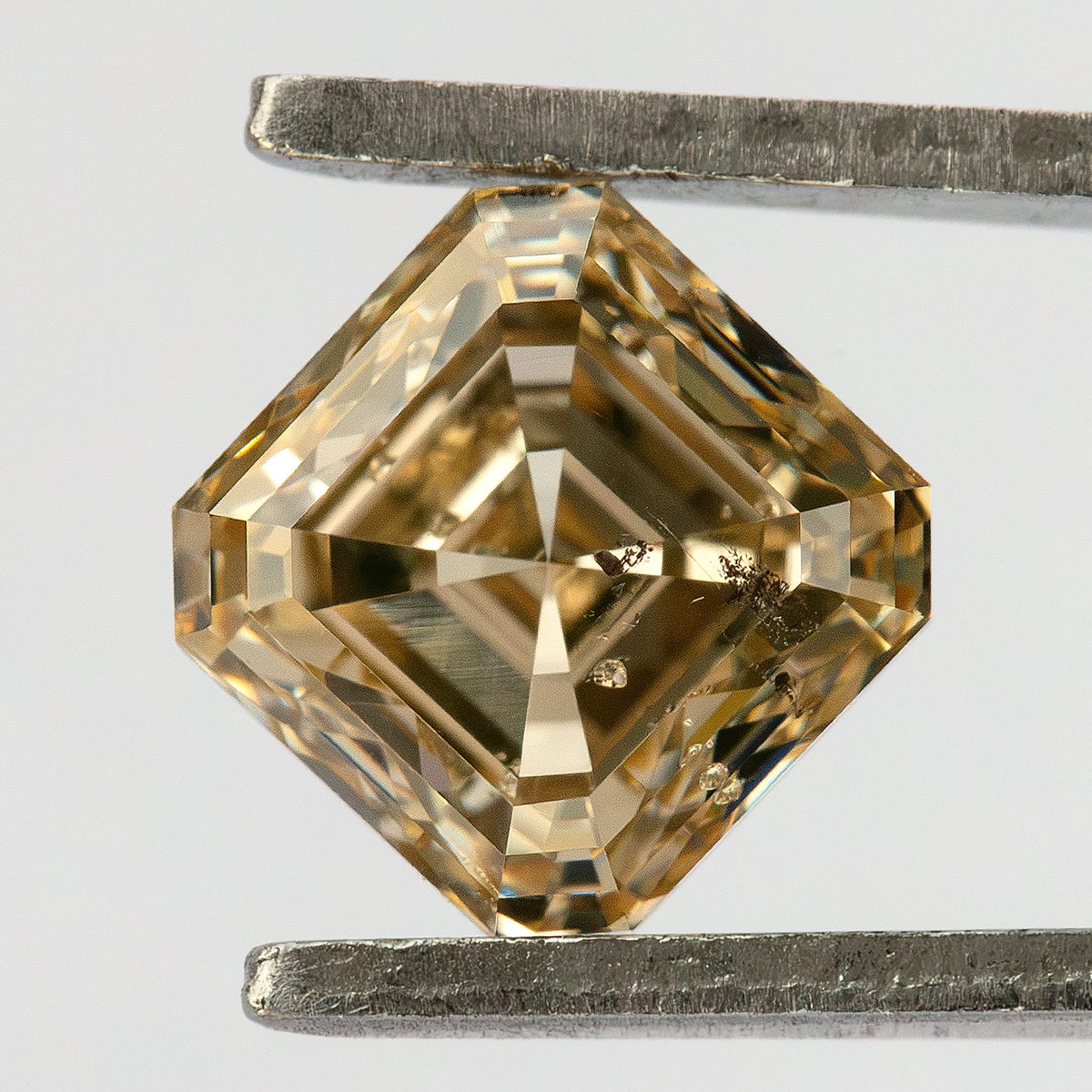 Pavilion-facing champagne diamond in tweezers, oriented diagonally with intersecting reverse facets visible.