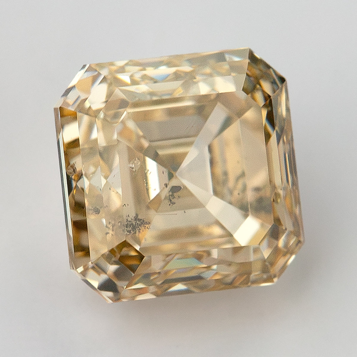 Light champagne diamond tilted on a pale background, showing a bright table reflection and internal dark characteristics.