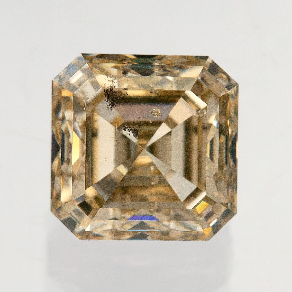Square face-up natural diamond showing warm gold-toned stepped reflections and dark internal features near the upper-left side.