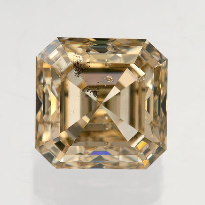 Square face-up natural diamond showing warm gold-toned stepped reflections and dark internal features near the upper-left side.