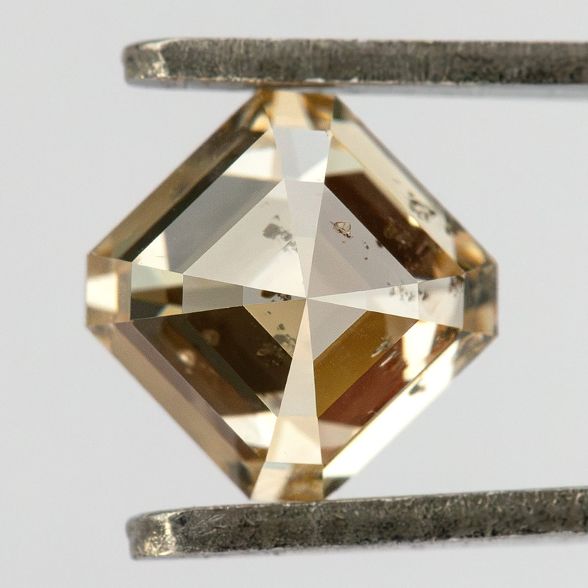 Close reverse view of the square diamond in tweezers, showing its pavilion facets and visible internal characteristics.