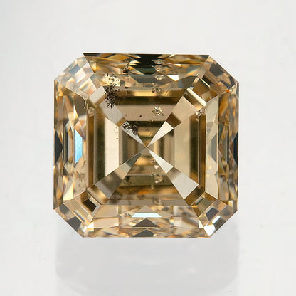 Square emerald-cut diamond photographed face-up, showing clipped corners, warm reflections and visible dark clarity features.
