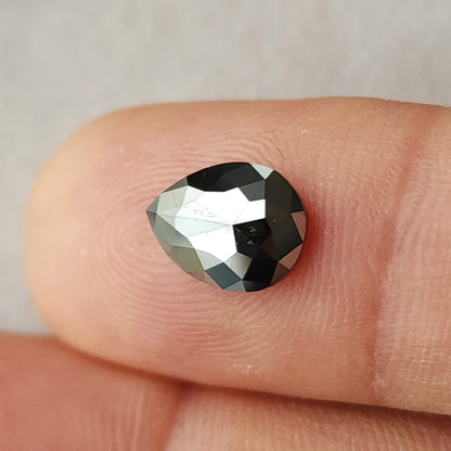 Angled view of the pear rose-cut black diamond resting on a fingertip, showing the rounded end, pointed tip and changing facet reflections.