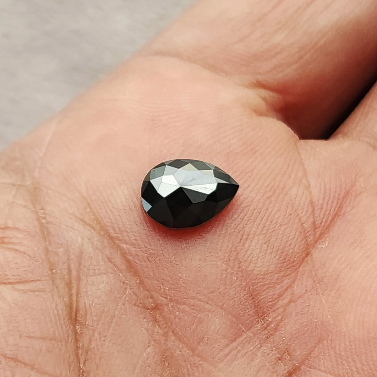 Wider hand-scale view of the black diamond resting on a fingertip, showing the pear outline, opaque body and bright central reflections.