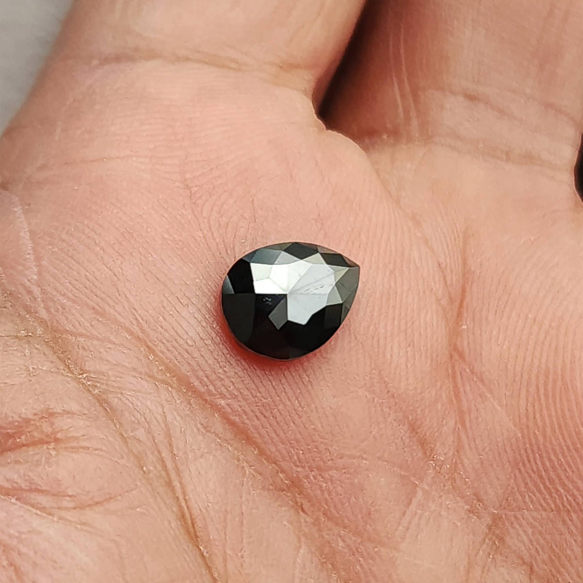 Wider palm-scale view of the pear rose-cut black diamond, showing its relative size, rounded end and pointed tip against the hand.