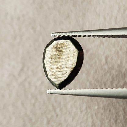 Reverse view of the pear rose-cut black diamond between tweezers, showing its flat back, pear outline and reflective surface.