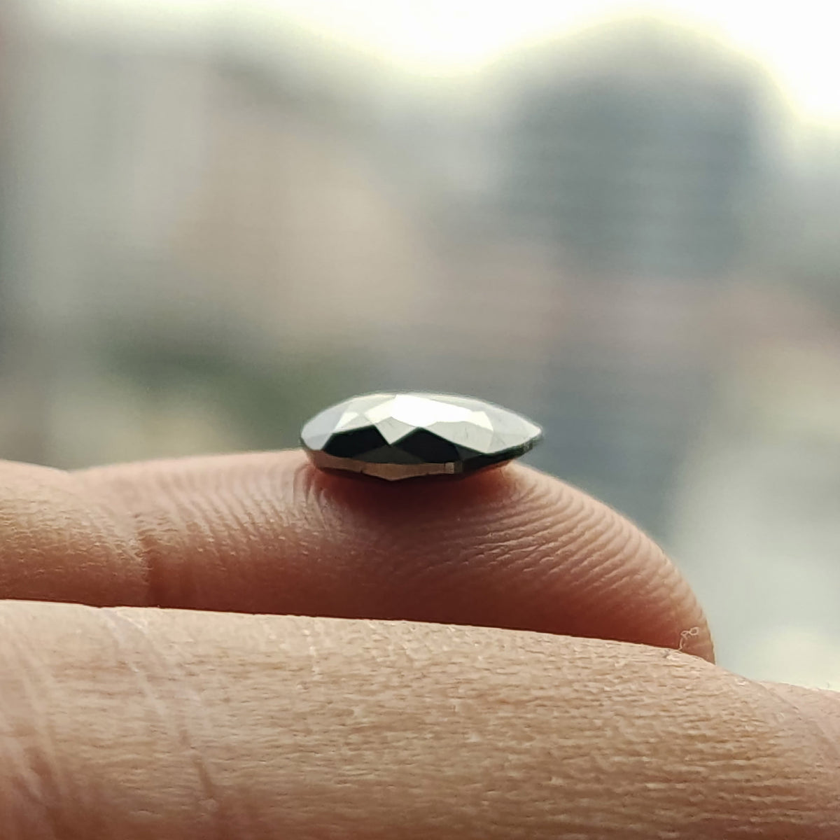 Side-profile macro of the pear rose-cut black diamond balanced on a fingertip, showing the low domed crown and flat-backed profile.