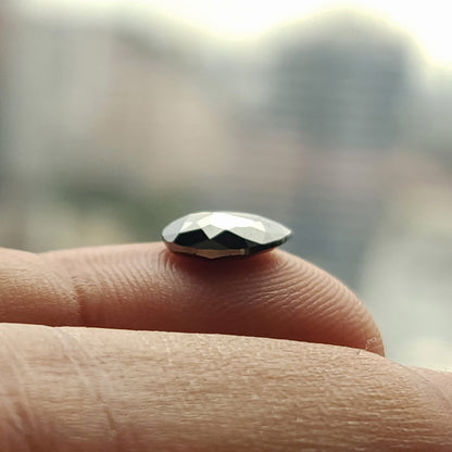 Side-profile macro of the pear rose-cut black diamond balanced on a fingertip, showing the low domed crown and flat-backed profile.