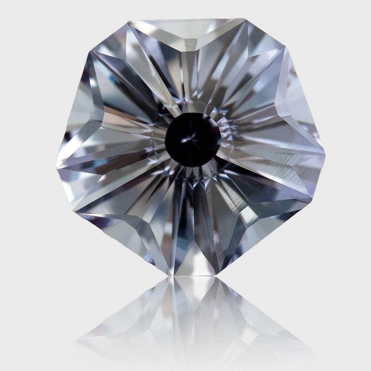 Face-up lab-grown sapphire with a five-sided outline, radial Hanami facets and pale gray-blue reflections on a light background.
