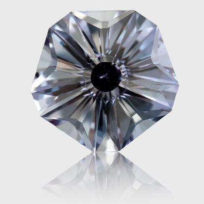 Face-up lab-grown sapphire with a five-sided outline, radial Hanami facets and pale gray-blue reflections on a light background.