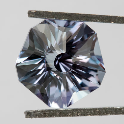 Face-up pentagon lab-grown sapphire held between horizontal tweezers, showing a different pattern of bright facets.