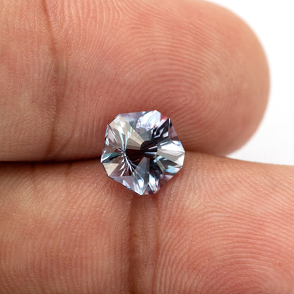 Face-up Hanami-cut sapphire resting between fingertips, with skin ridges showing its scale.