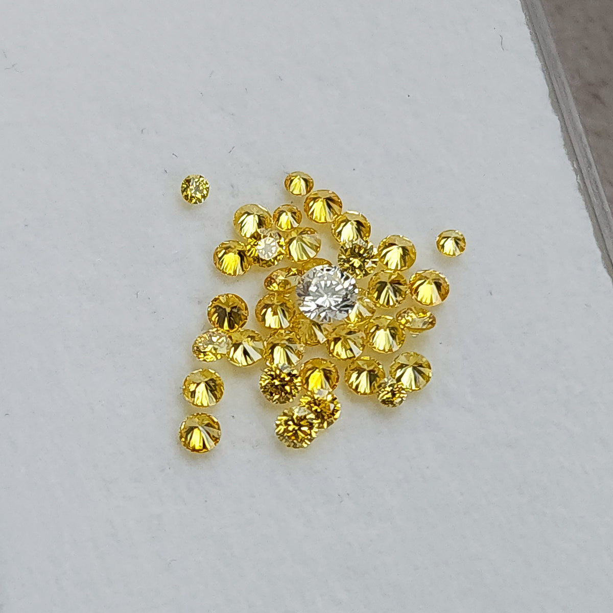Loose yellow diamond cluster on a pale surface with an excluded white comparison diamond.