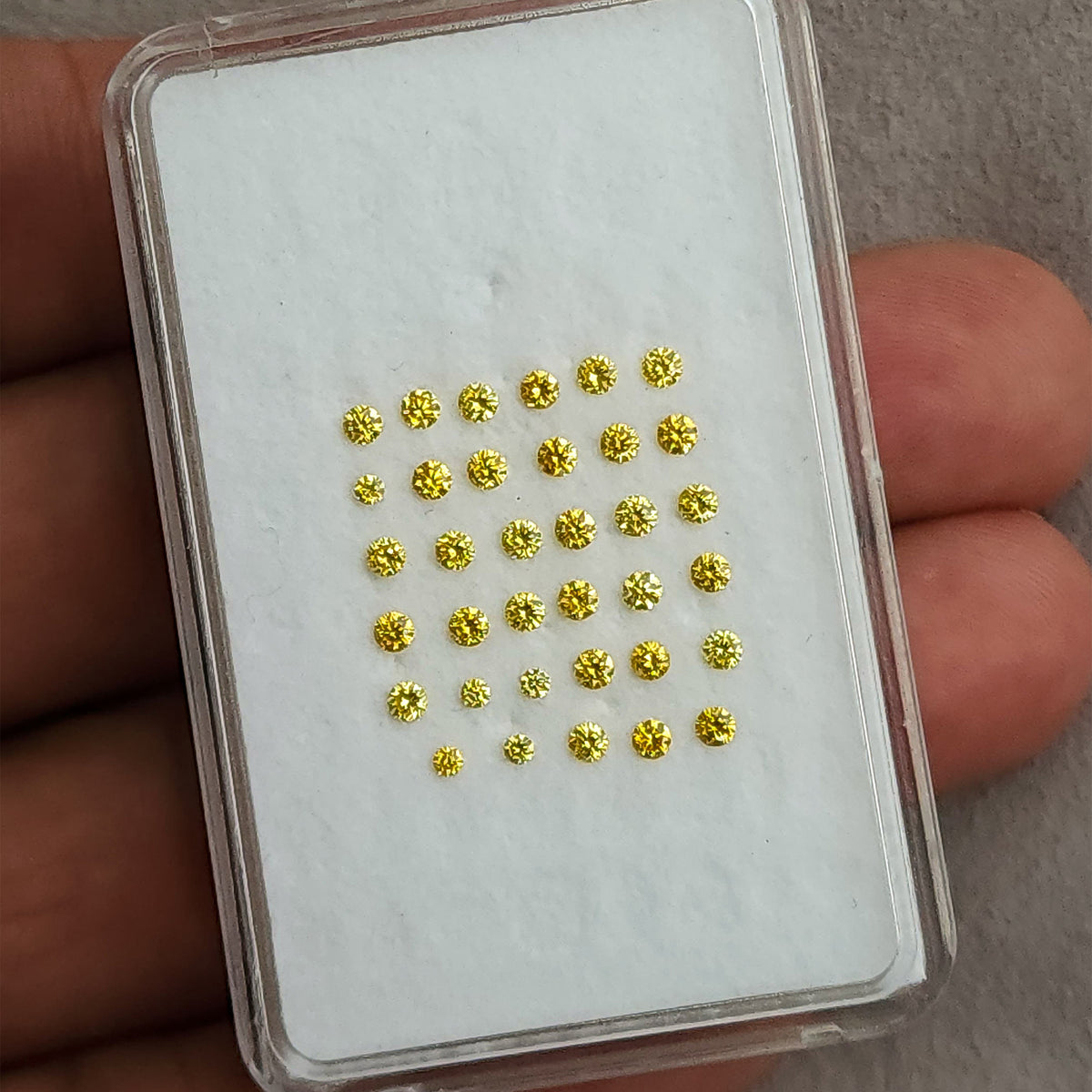 Rows of yellow diamonds inside a rectangular case held against a palm for scale.
