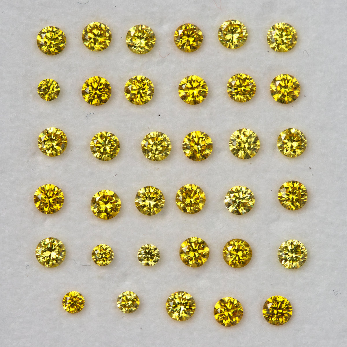 Closer face-up display of yellow diamonds in even rows on a pale background.