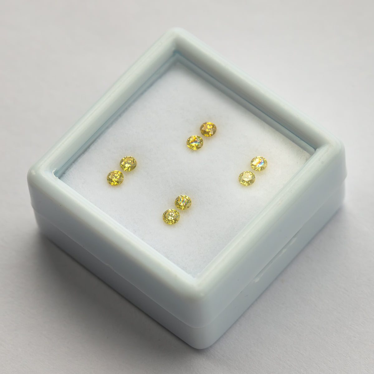 Four yellow diamond pairs in an angled white display tray on a pale surface.