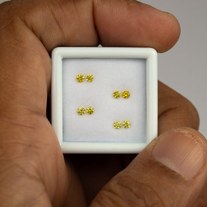 White tray of four yellow diamond pairs held between fingers, showing size context.