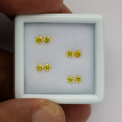 Close face-up view of four yellow diamond pairs with fingers at the tray edges.