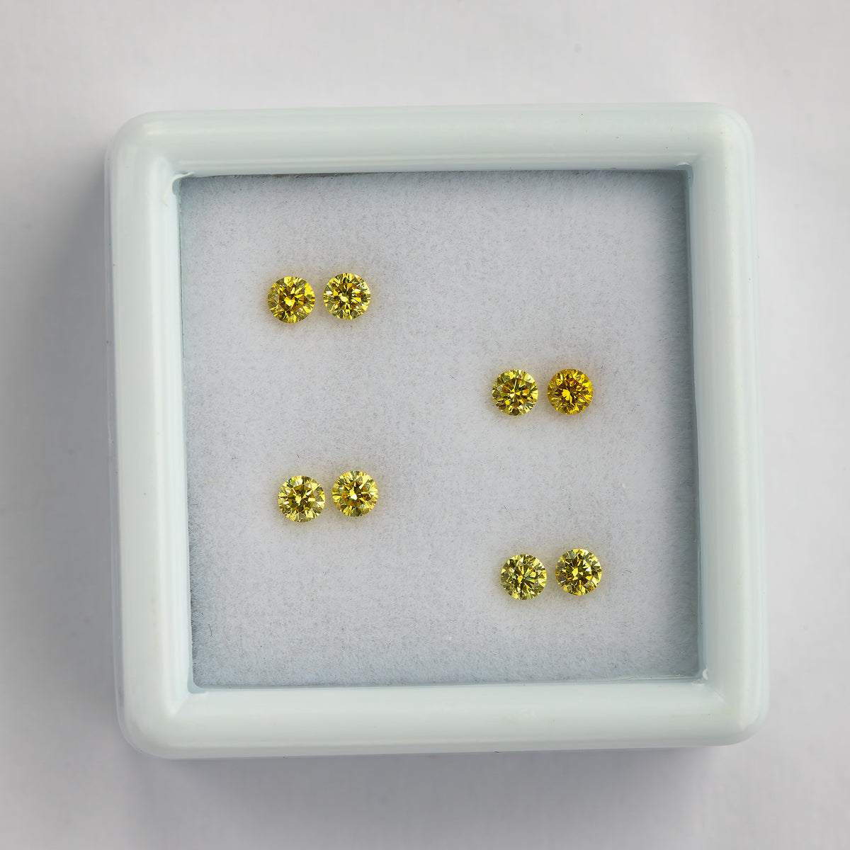 Overhead view of four yellow diamond pairs arranged inside a white tray.