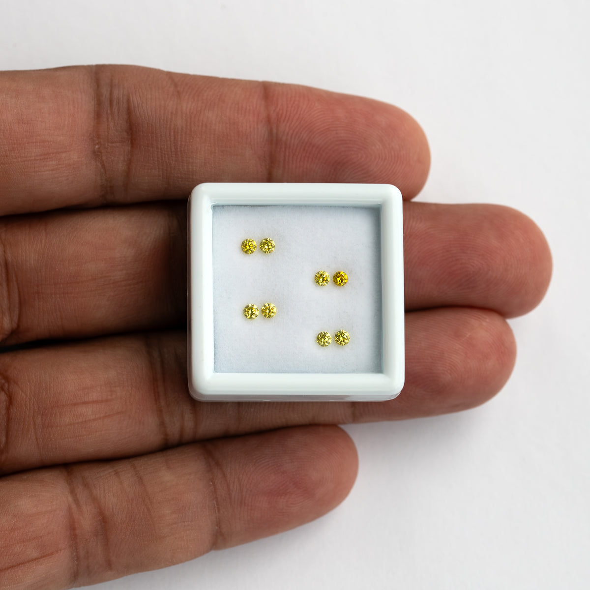 Four yellow diamond pairs in a small white tray on a palm for scale.