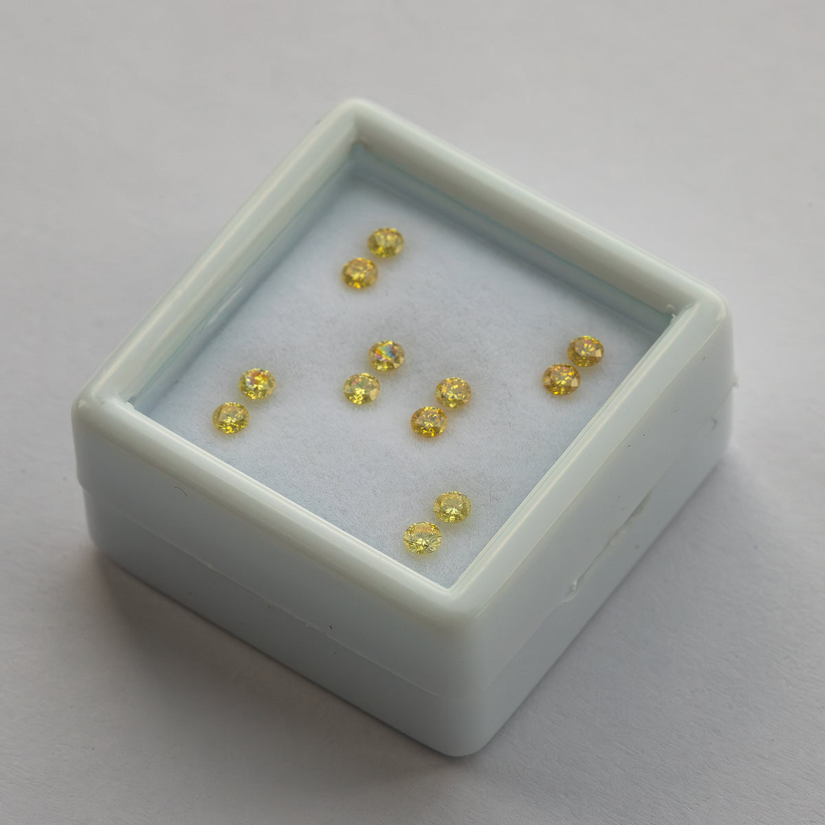 Six yellow diamond pairs in a tilted white display tray on a pale surface.