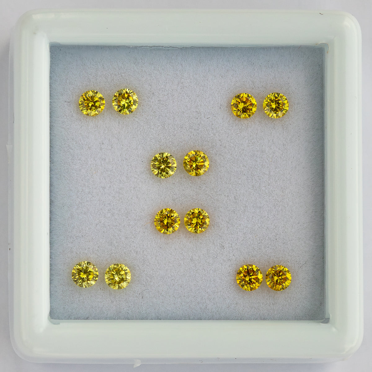 Centered overhead view of six yellow diamond pairs in a white tray.