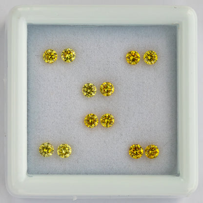 Centered overhead view of six yellow diamond pairs in a white tray.