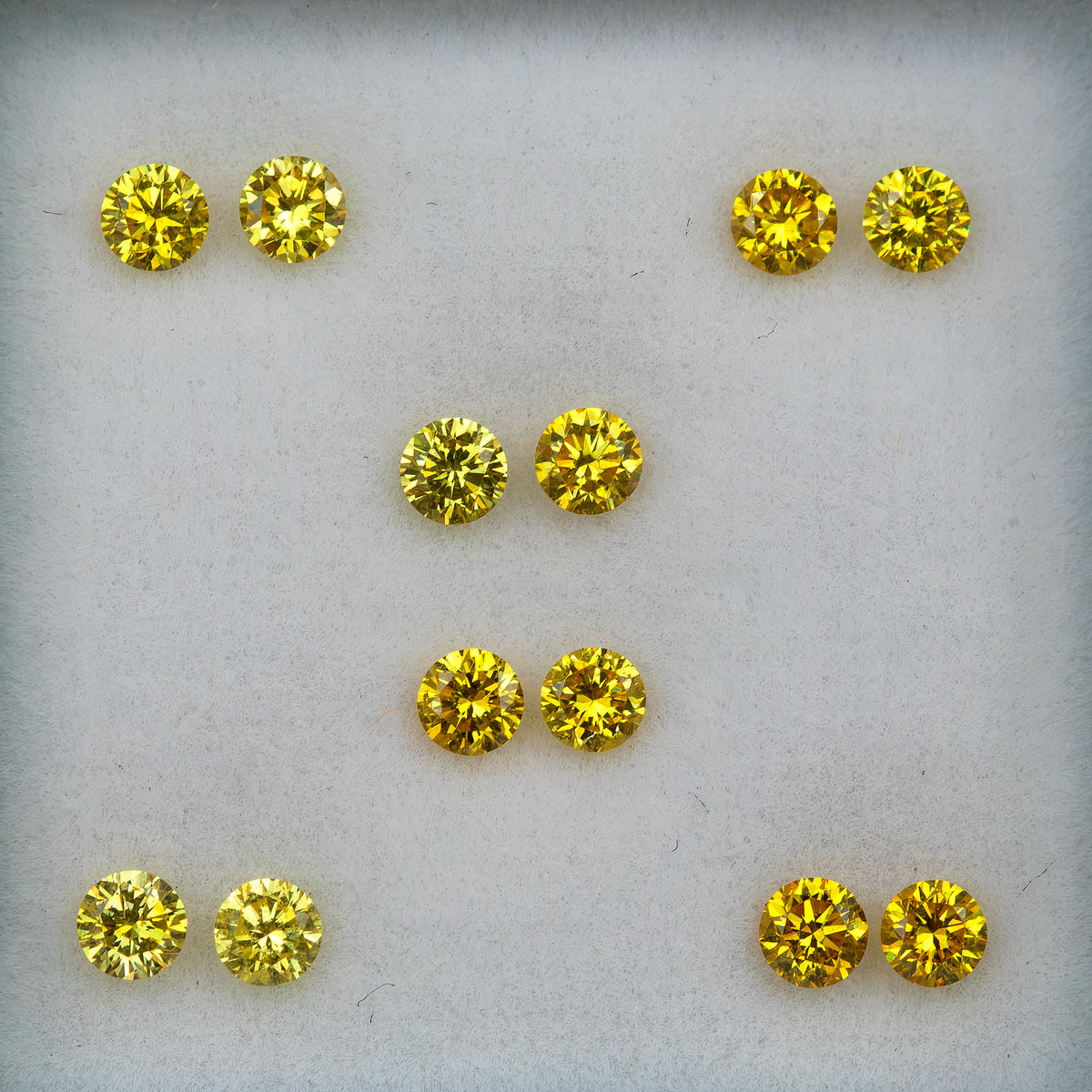 Face-up comparison of six yellow diamond pairs arranged on a pale surface.