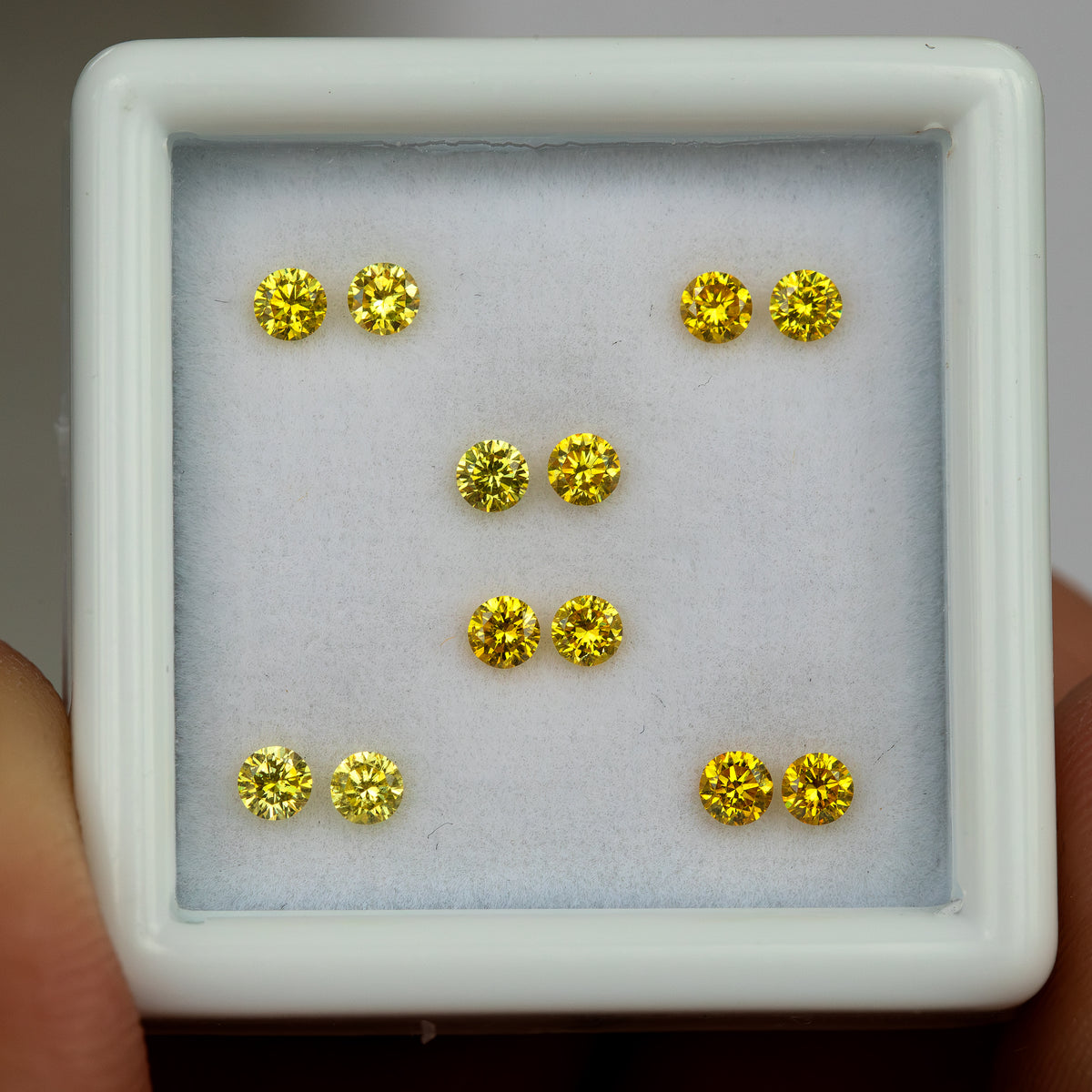 Close front view of the six yellow diamond pairs in a tray held by fingers.