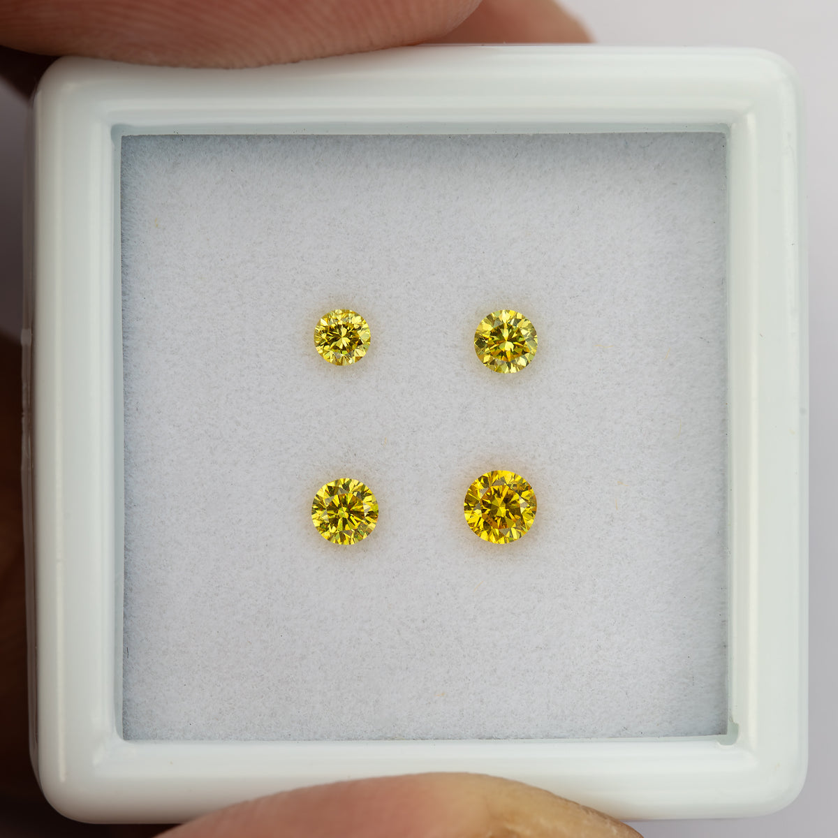Four yellow round diamonds in a white tray held close between fingers.