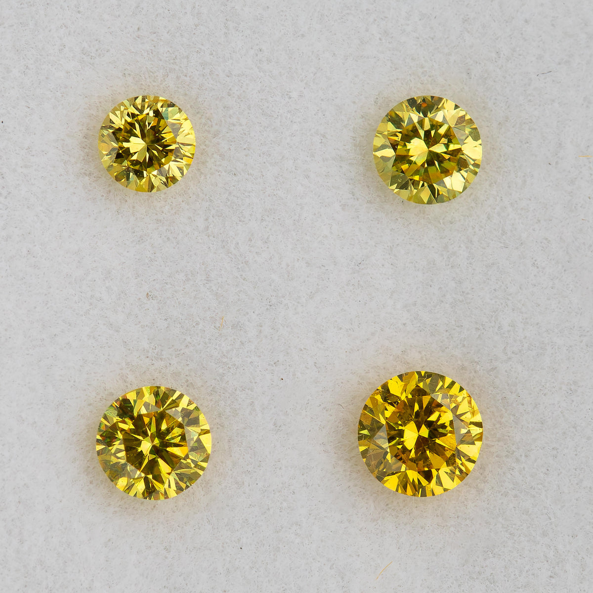 Close face-up comparison of four individual yellow round brilliant diamonds.
