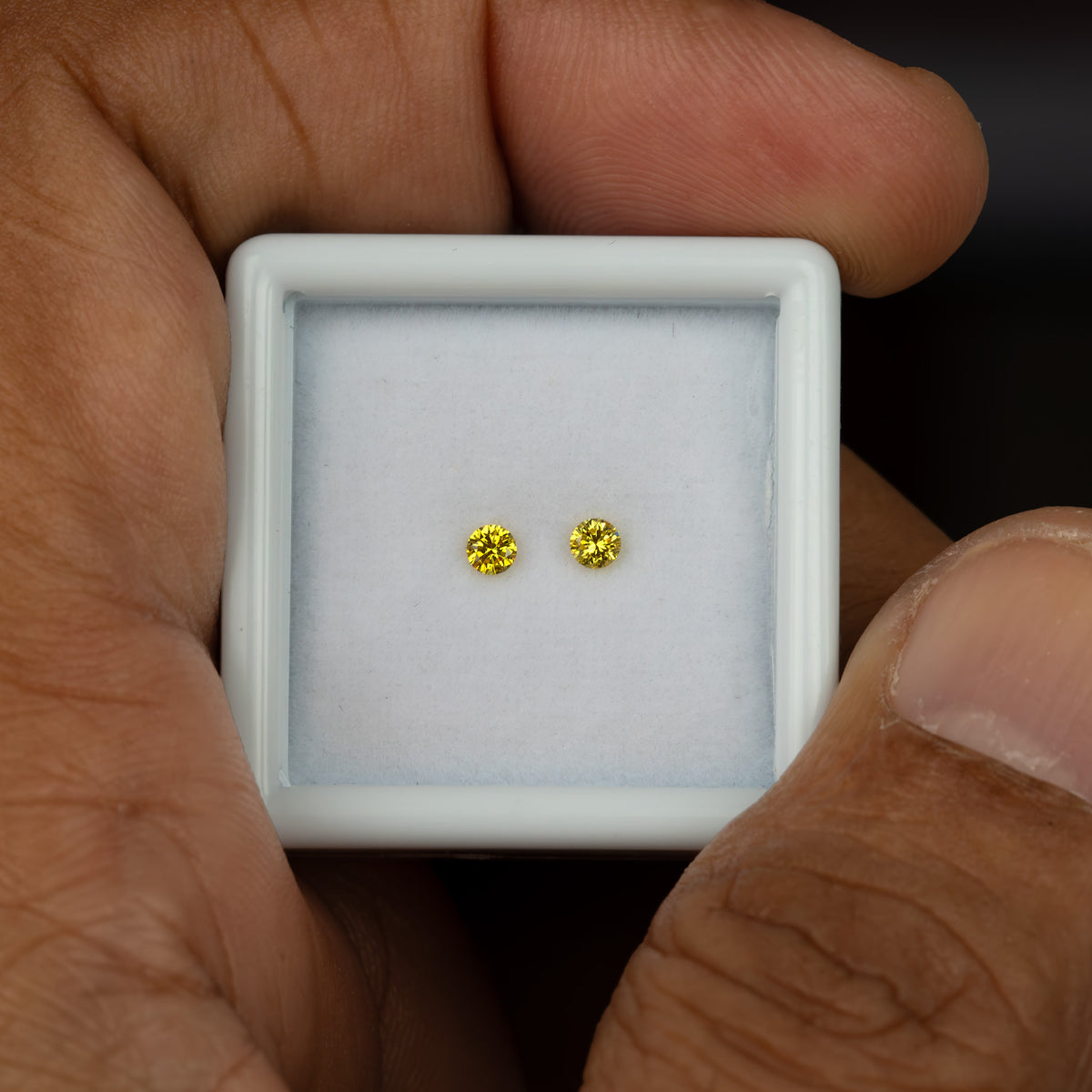 Handheld view of the two matched canary yellow round diamonds