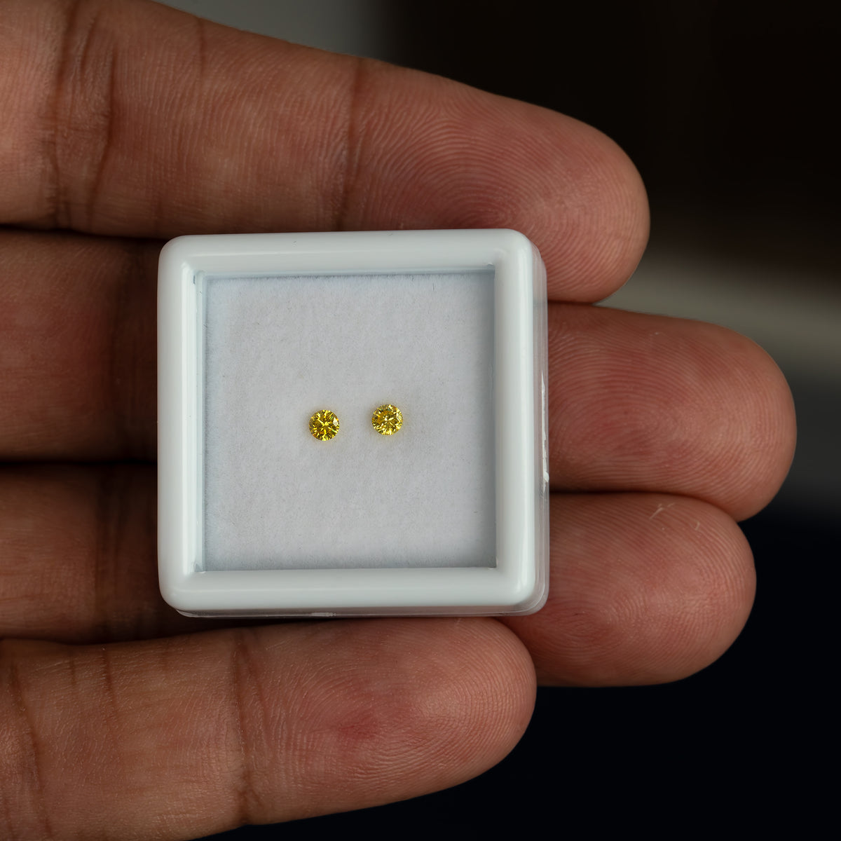 Matched yellow diamond pair shown on a palm for scale